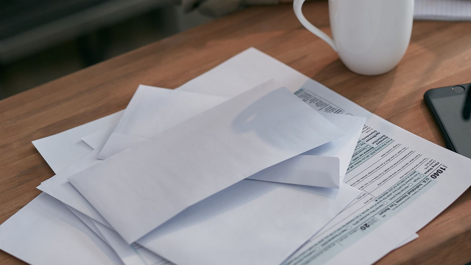 Workspace with envelopes, IRS tax return forms, and a coffee cup on a wooden table